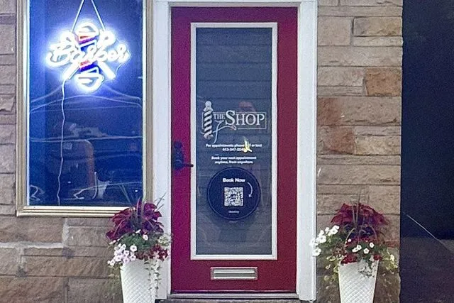 The red front door of The Shop, with a neon Barber sign in the window
