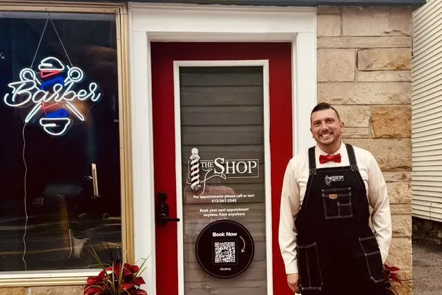 Barber John Chapman smiling outside the red front door of The Shop in Pittsfield